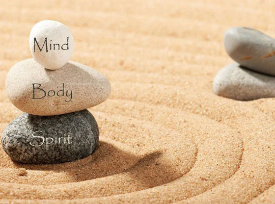 Trys sukrauti akmenys su užrašais „Mind“, „Body“, „Spirit“ ant grėbliuoto smėlio