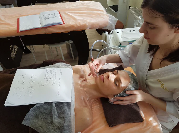 Grožio terapeutė atlieka klientės veido procedūrą, šalia užrašų lapas