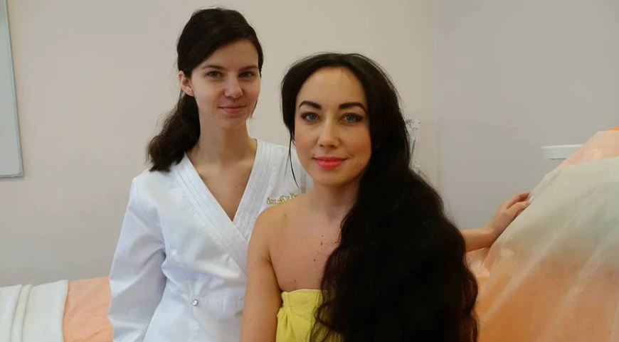 Grožio terapeutė baltu chalatu su modele ilgais tamsiais plaukais