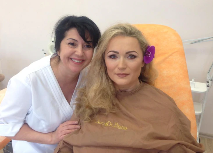 Grožio terapeutė su šviesiaplauke modele, papuošta gėle plaukuose