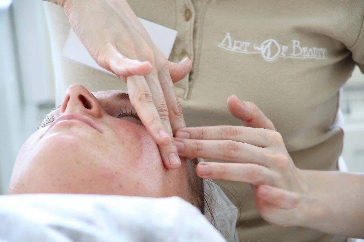 Masažuotojas „Art of Beauty“ uniforma atlieka gulinčios moters veido masažą