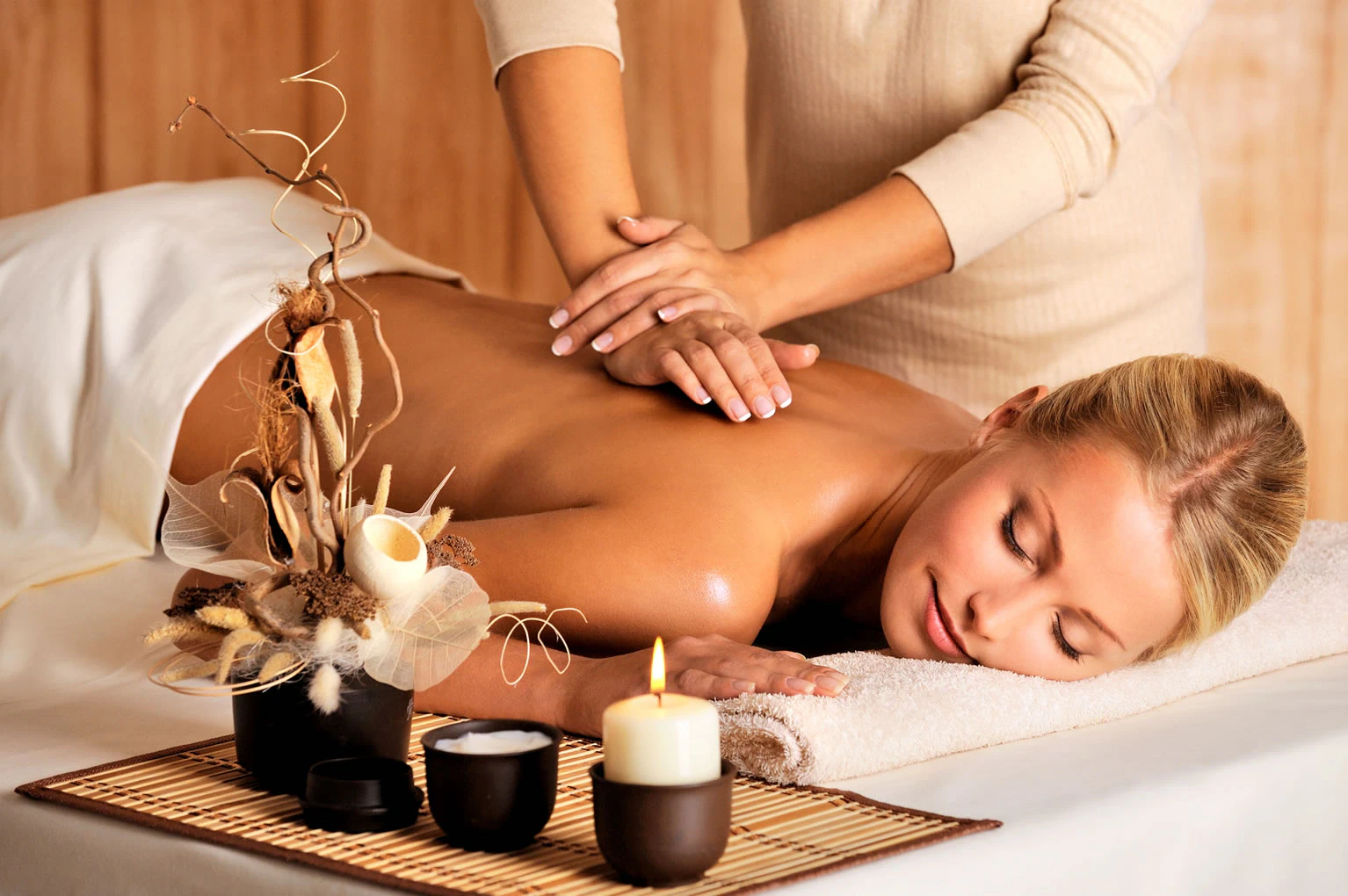 SPA nugaros masažas su žvakėmis ir dekoracijomis šalia masažo stalo SPA nugaros masažas su žvakėmis ir dekoracijomis šalia masažo stalo