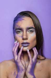 Modelė su violetiniu kūrybiniu veido ir rankų makiažu