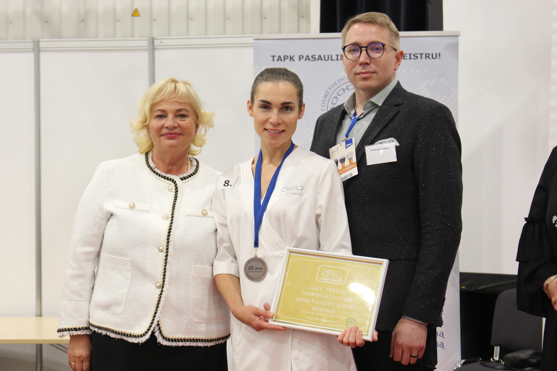 Konkurso prizininkė su medaliu ir diplomu tarp dviejų apdovanojimų teikėjų