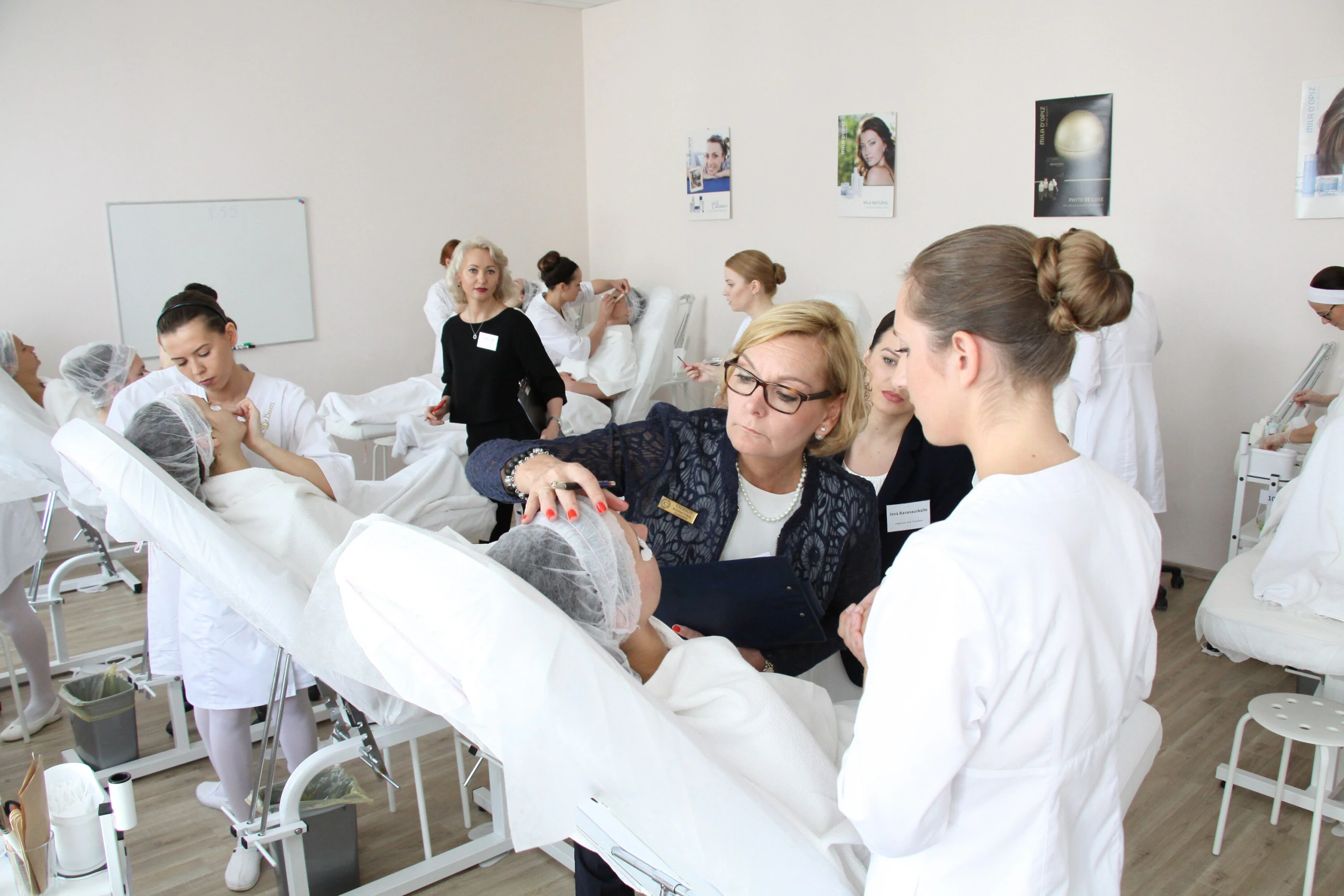Egzaminuotoja tikrina dalyvės atliekamą veido procedūrą per CIDESCO egzaminą Egzaminuotoja tikrina dalyvės atliekamą veido procedūrą per CIDESCO egzaminą