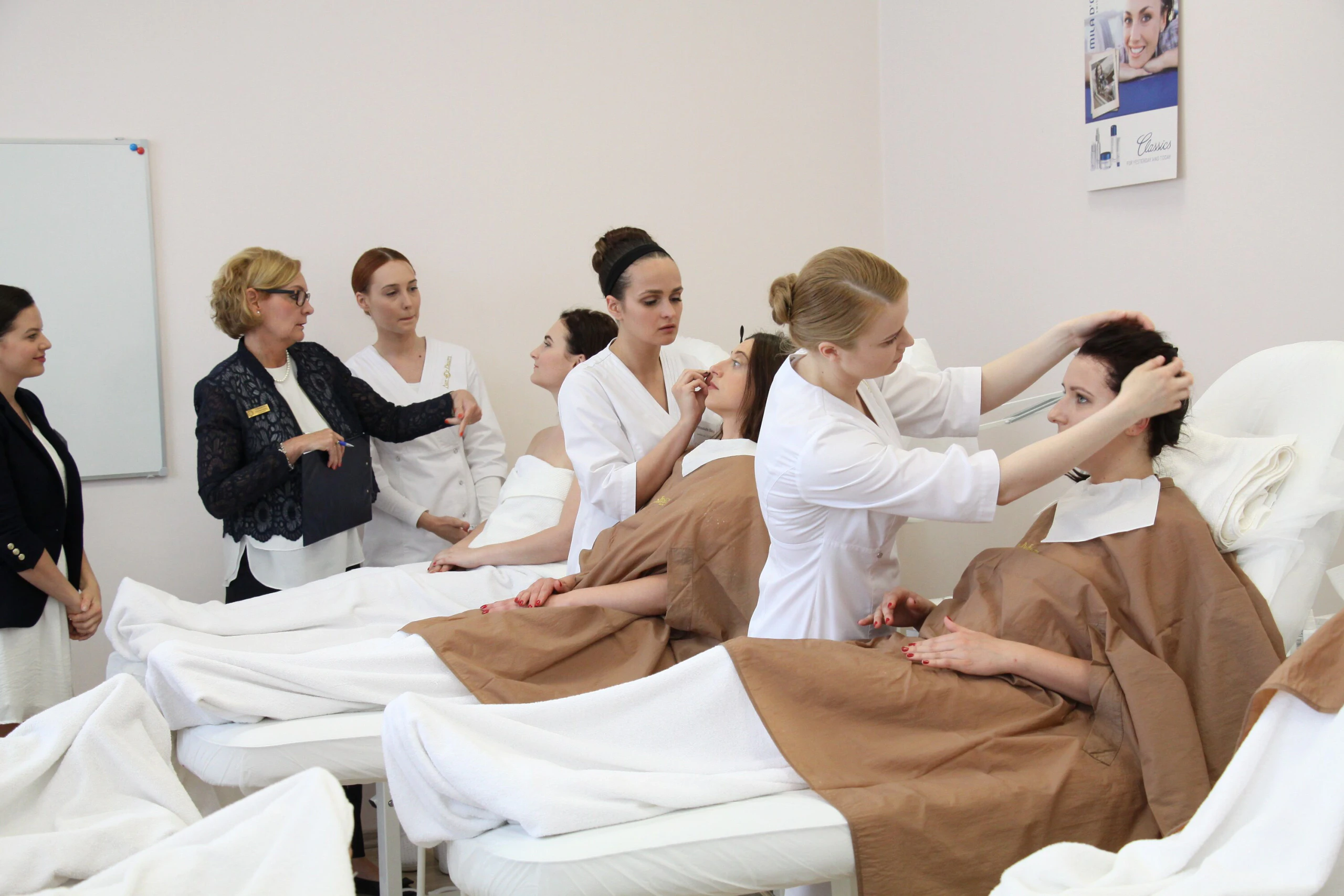 Egzaminuotoja stebi dalyves, ruošiančias klientes makiažo užduočiai Egzaminuotoja stebi dalyves, ruošiančias klientes makiažo užduočiai
