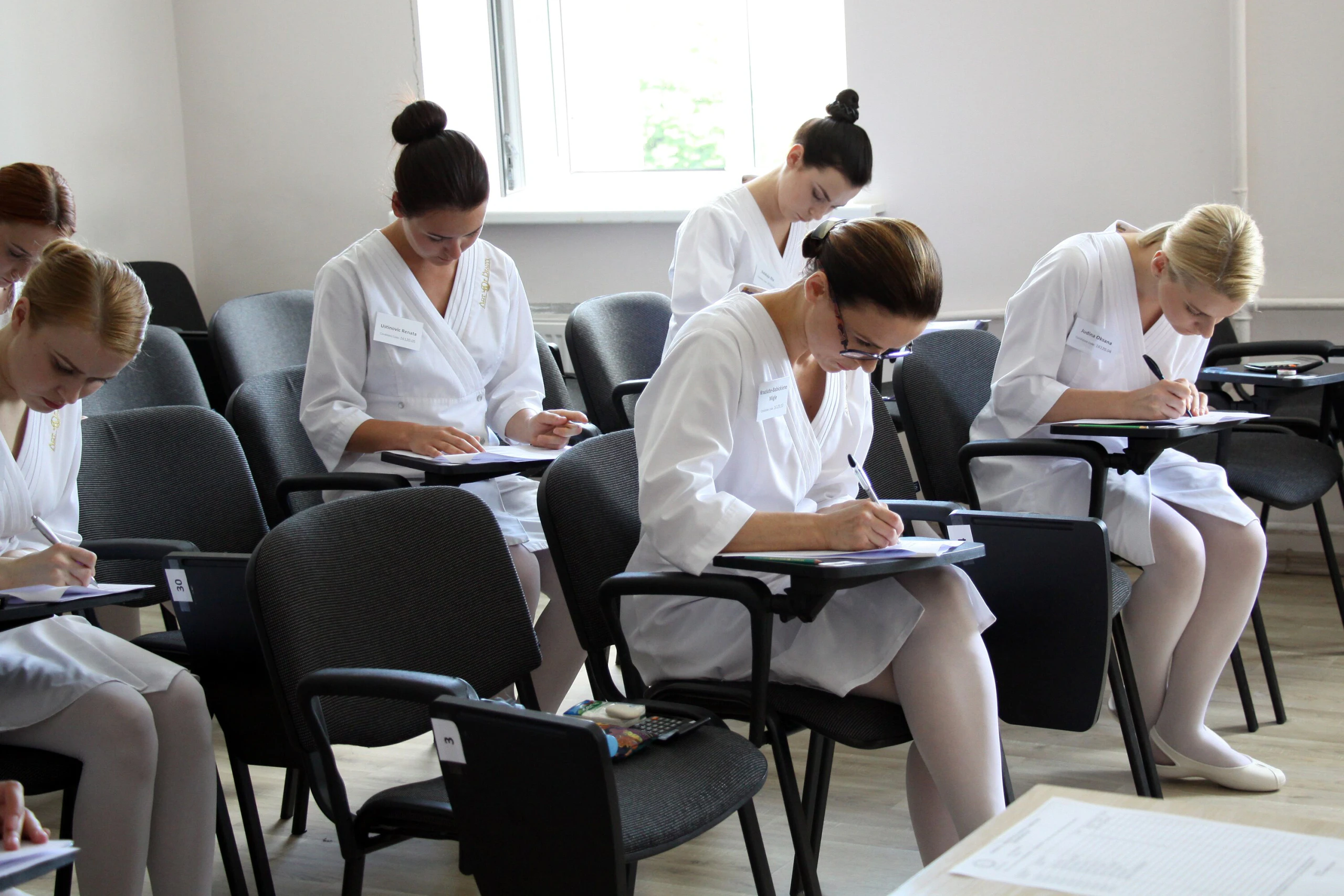 CIDESCO egzamino dalyvės baltomis uniformomis sprendžia teorinį testą CIDESCO egzamino dalyvės baltomis uniformomis sprendžia teorinį testą