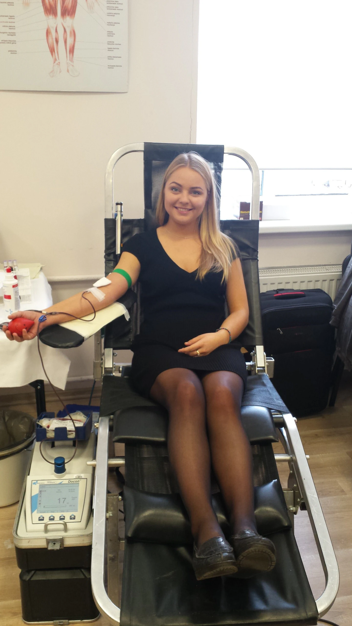 Jauna donorė juoda suknele donoro kėdėje per kraujo donorystės akciją