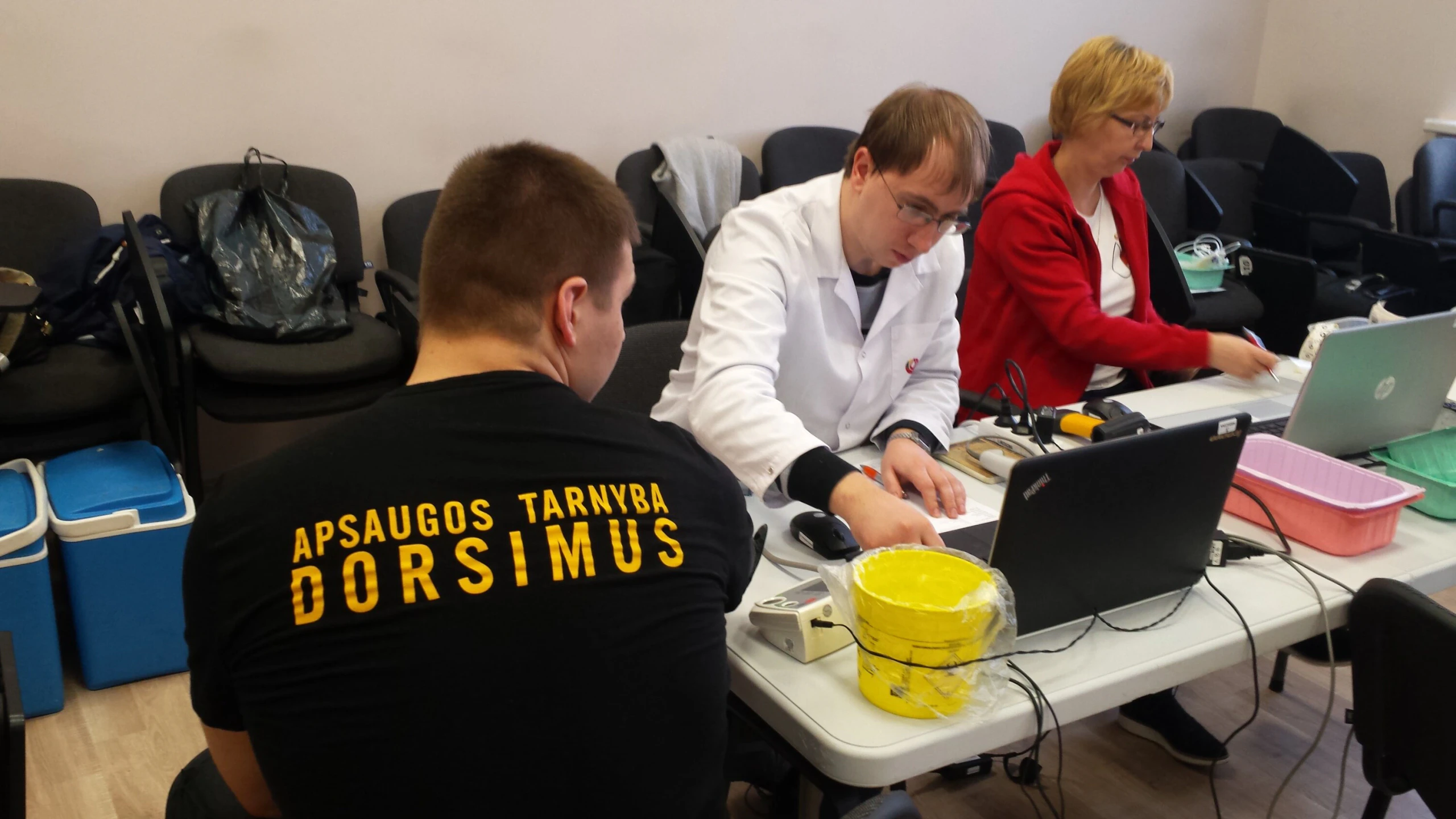 Gydytojas ir medikė registruoja donorą prie stalo per kraujo donorystės akciją
