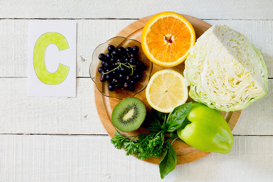 Daug vitamino C turinčios daržovės ir vaisiai ant medinio padėklo
